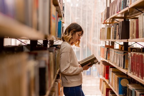 Young lady reading book in Library aisle
